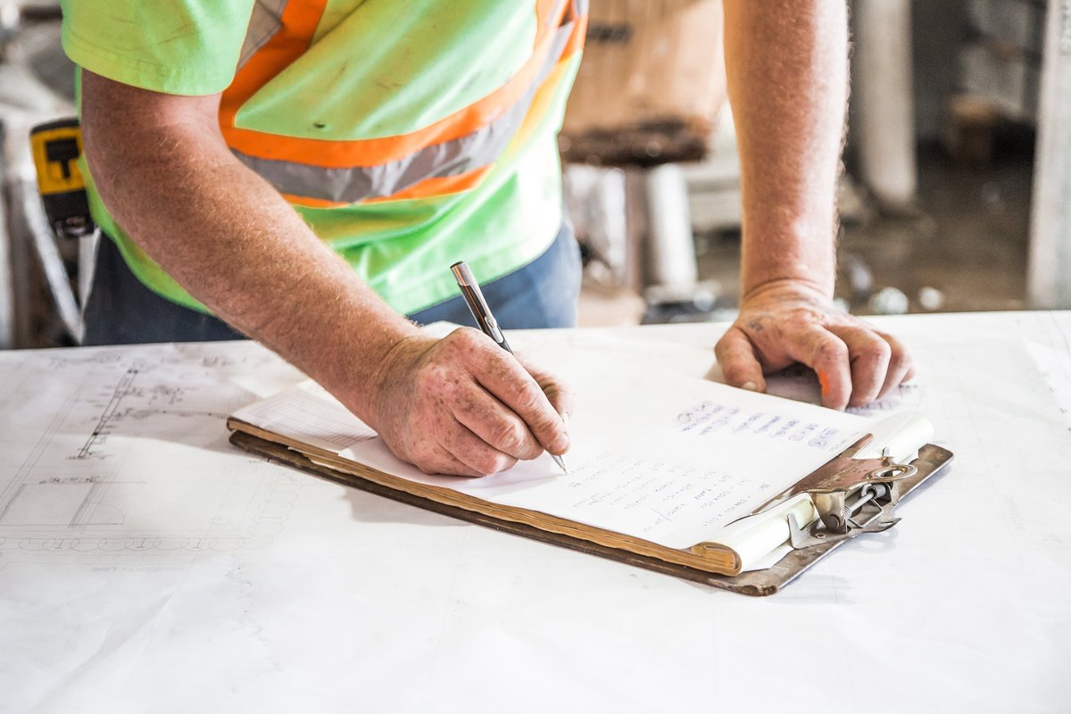 A worker writing on a clipboard over building plans