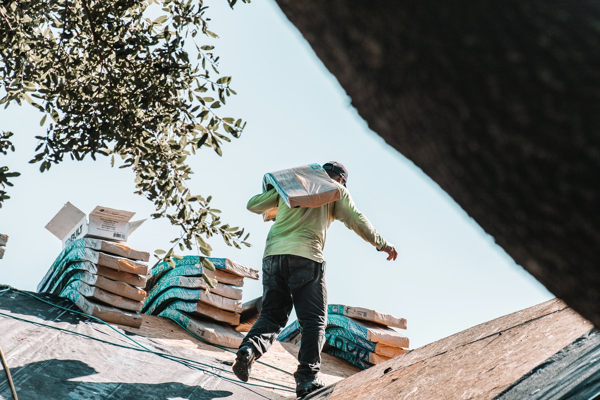A roofer carrying a bundle of shingles across a roof
